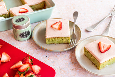 Two pieces of matcha tres leches cake with strawberry frosting on kitchen counter.