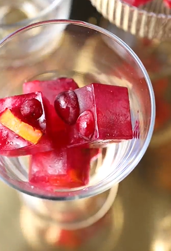 Up close of red Merry Maker's ice cubes with cranberries and orange peel within ice cube.