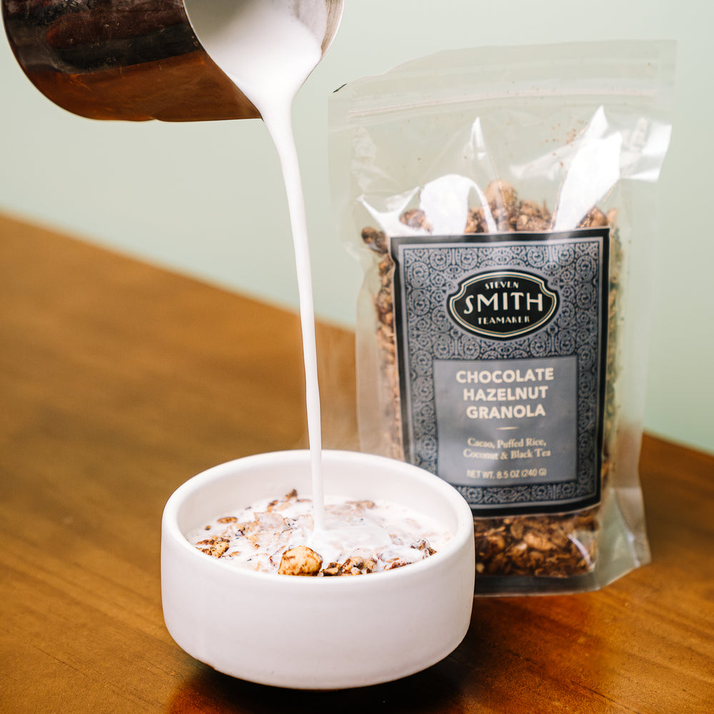 Milk being poured into a white bowl of granola on wooden table.
