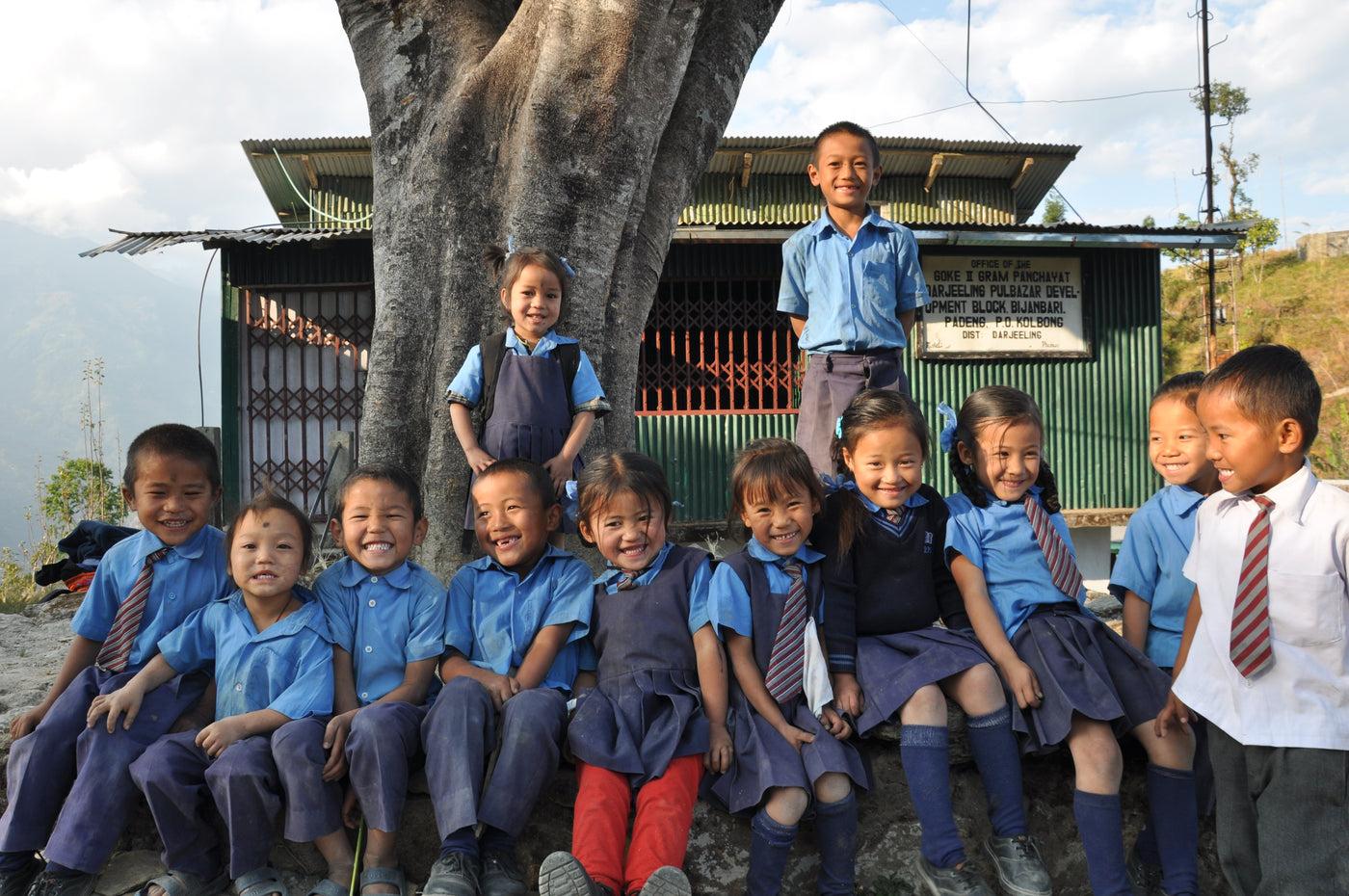 Group of Himalayan school children in blue uniforms laughing in front of schoolhouse.