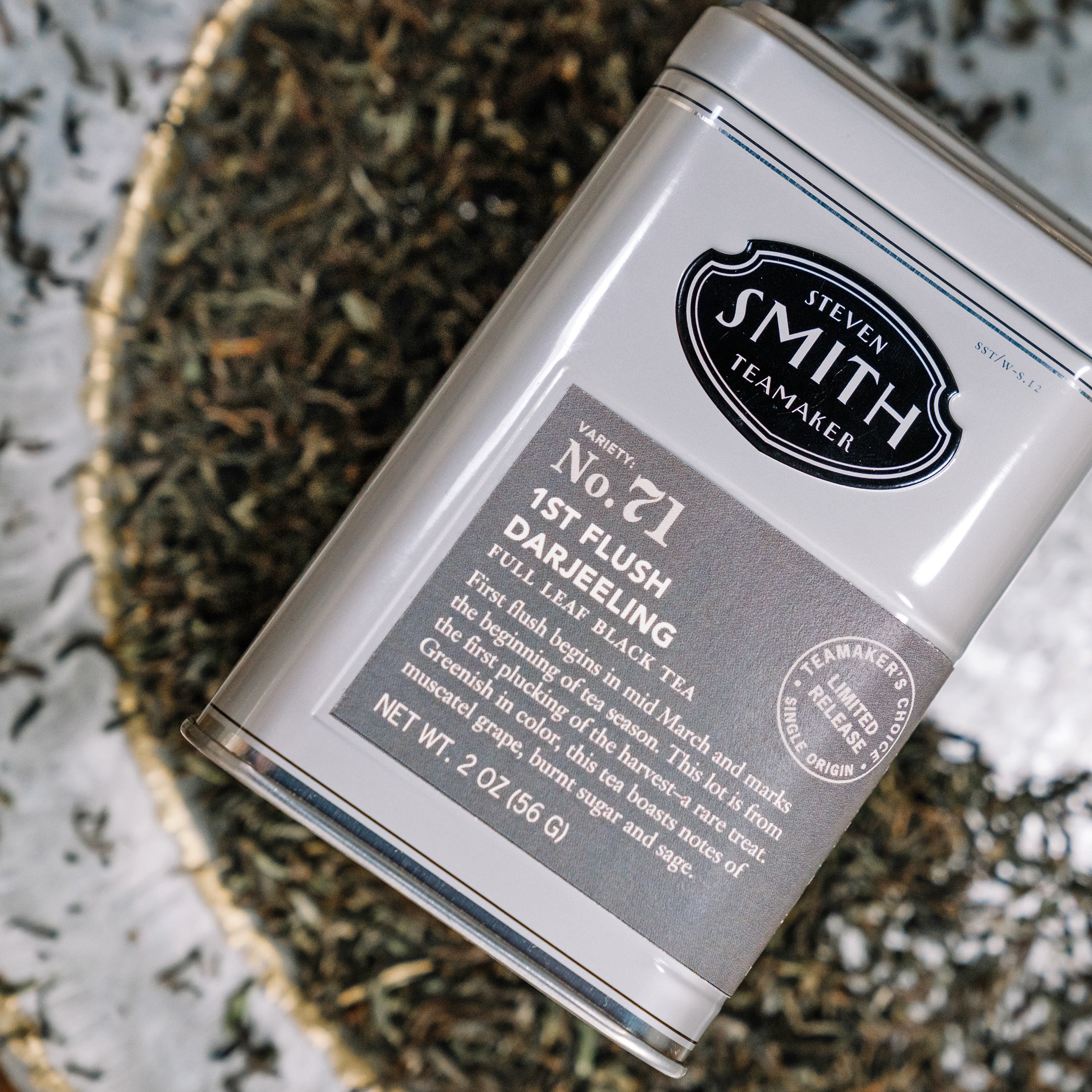 Close up tin of 1st flush Darjeeling tea surrounded by loose tea.