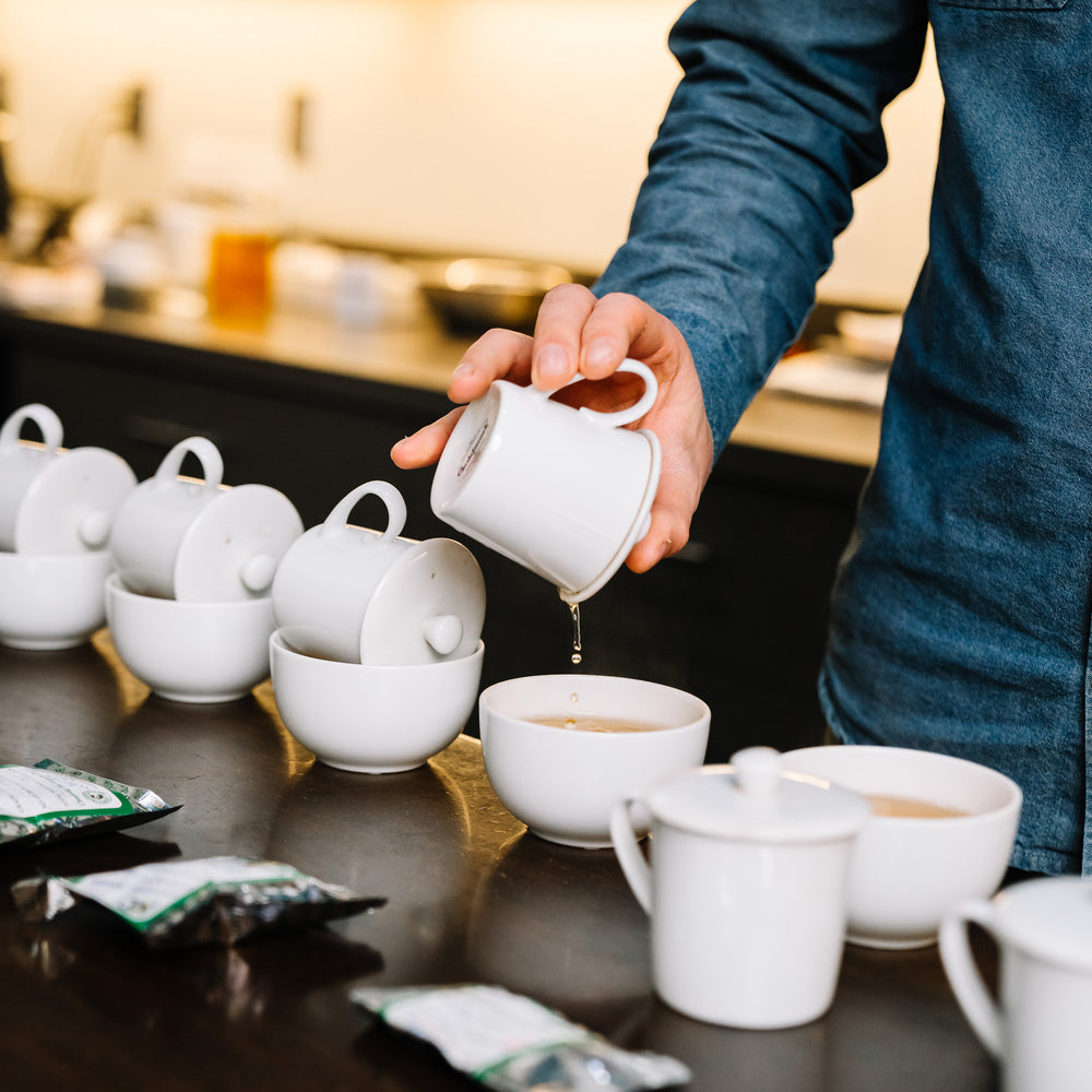 Hand holding tea strainer above sampling cup to strain tea.