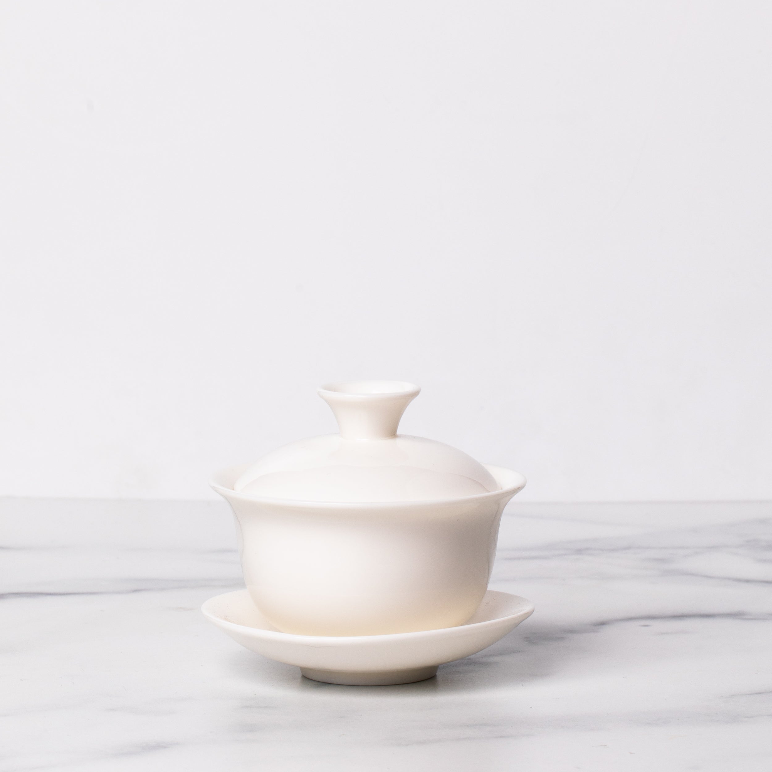 White lidded circular porcelain bowl on circular saucer.