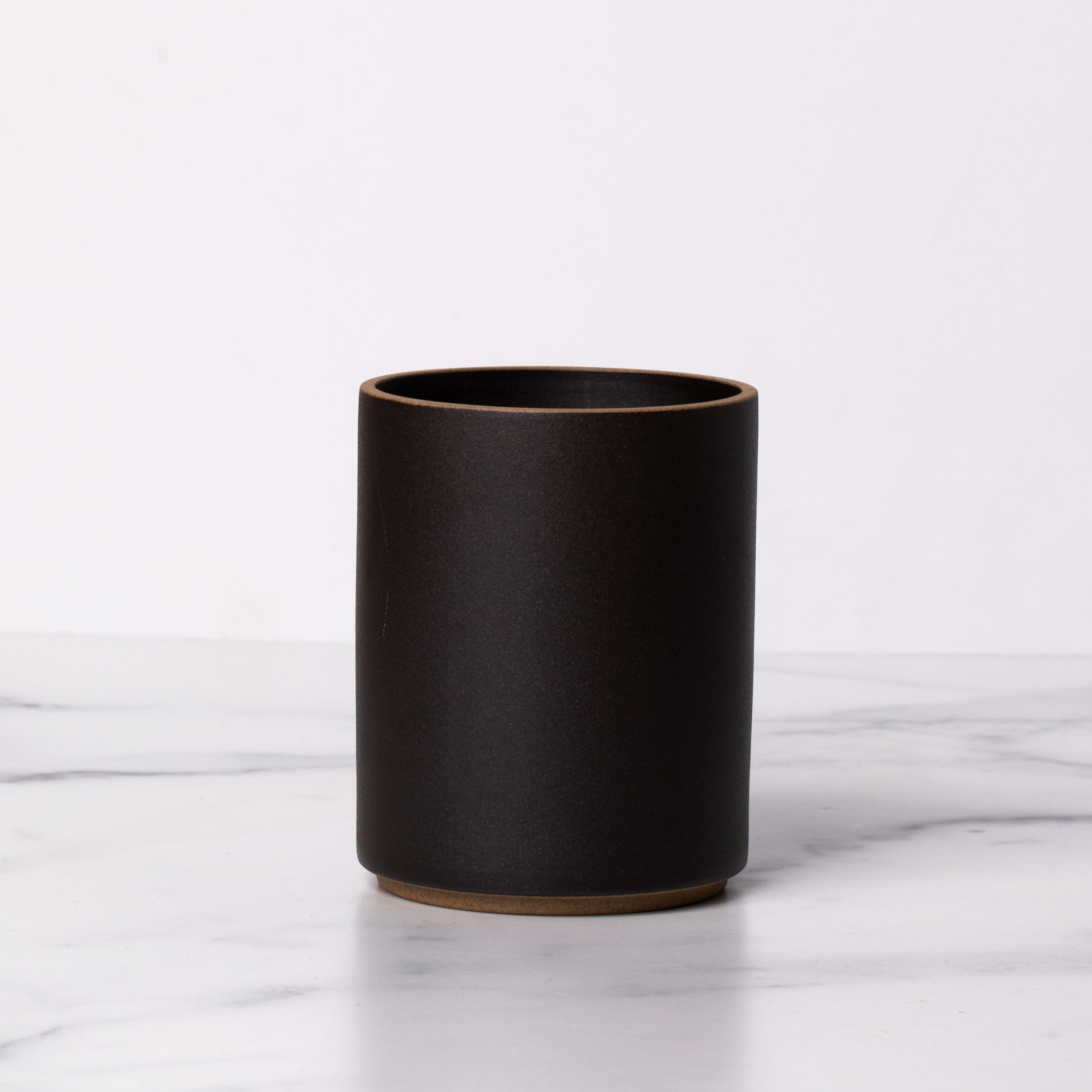 A black porcelain tea tumbler with no handle on a marble background.