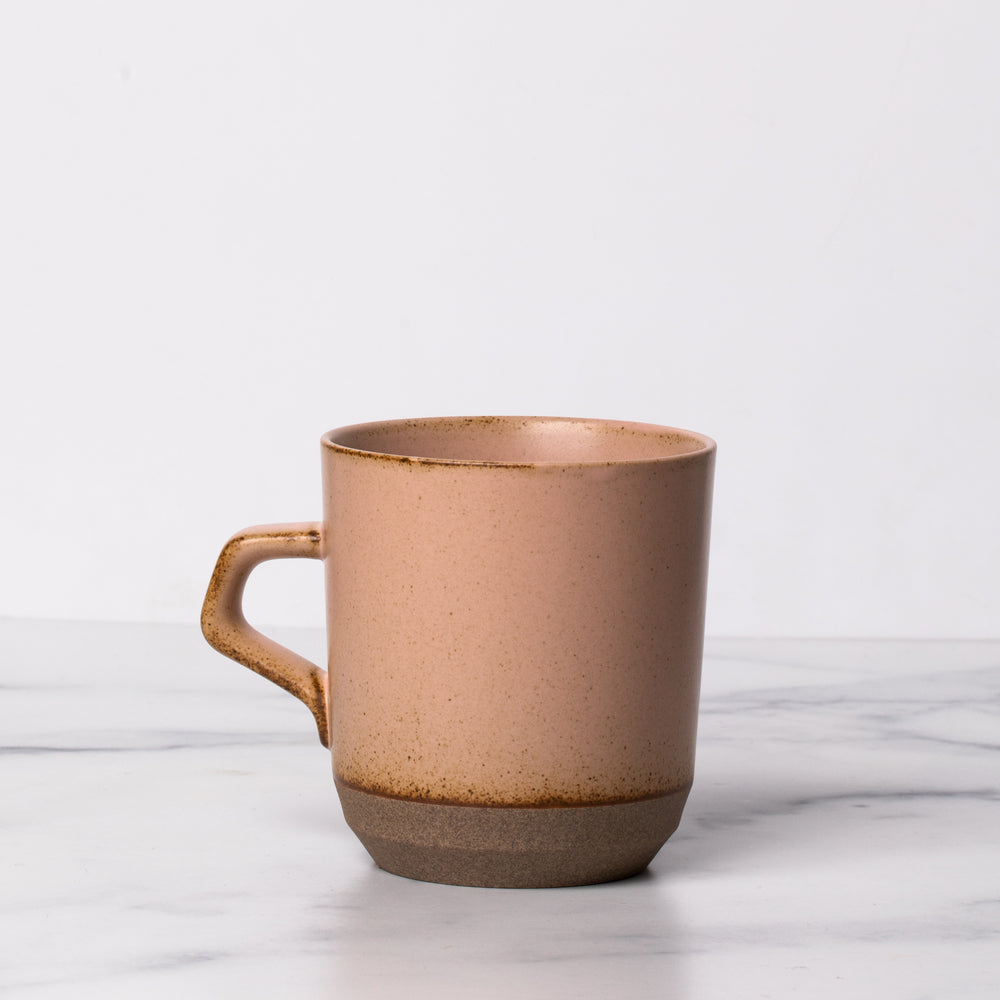 Pink ceramic mug with a handle on marble background.