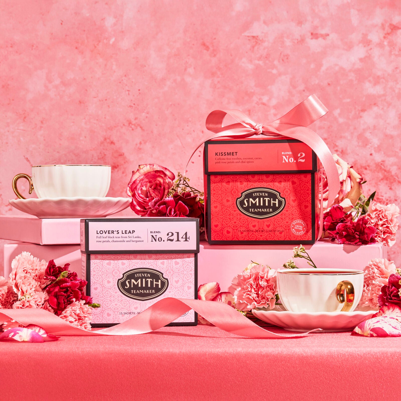 Pink box of Lover's Leap and rose-red box of Kissmet in a pick tea party scene with ornate teacups, flowers and pink ribbons.
