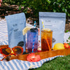 Two packages of Smith Tea with iced tea drinks on a wooden tray outdoors.