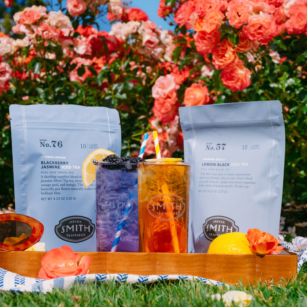 Two packages of Smith Tea with two iced teas on a wooden tray in a garden setting.
