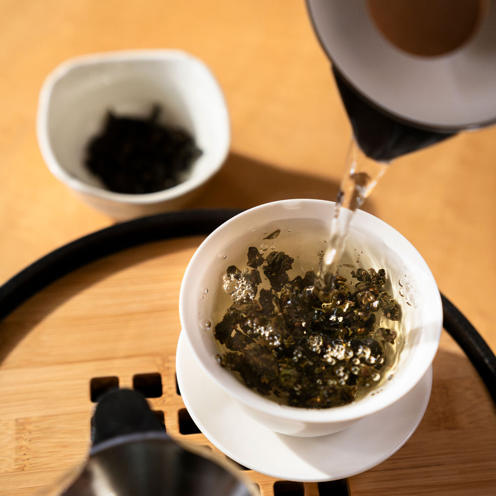 Water being poured into porcelain cup filled with oolong tea.