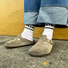White crew socks with Smith Teamaker written around the ankle in black block letters worn with Birkenstocks and jeans.