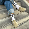 Person sitting on stairs wearing white crew socks with Smith Teamaker written around the ankle in black block letters.