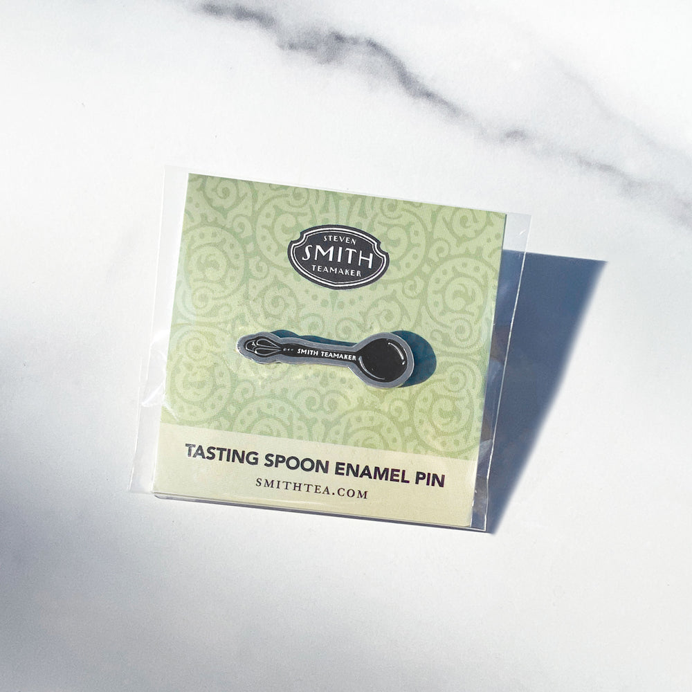 Enamel pin in the shape of a tasting spoon with "Smith Teamaker" inscribed on the spoon handle on a green card with text "Tasting Spoon Enamel Pin".