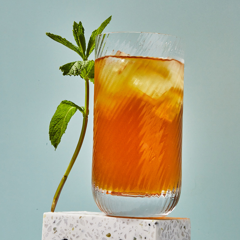 Iced glass filled with brown mint iced tea and a mint sprig.