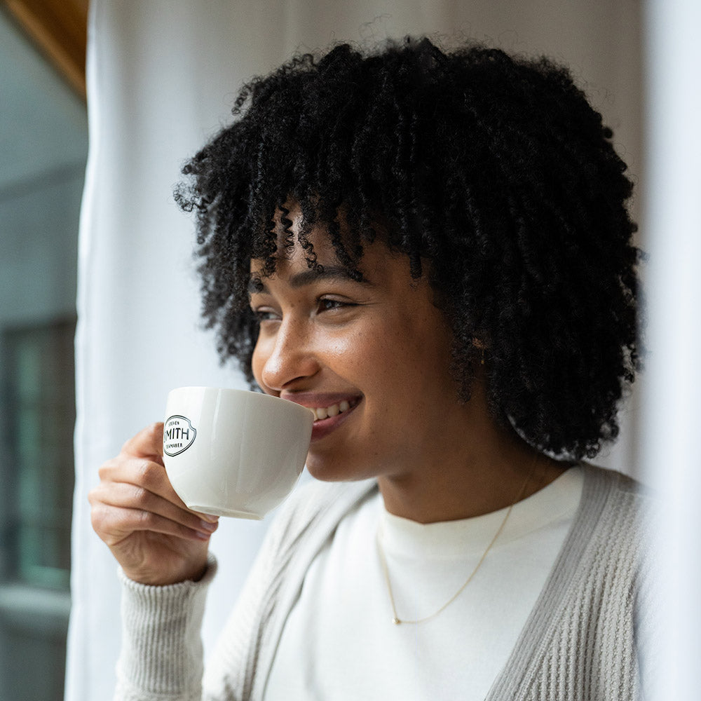 woman looking out a window drinking a cup of tea.