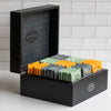 Wooden black box on kitchen counter with lid opened to showcase green, black and orange sachets of tea.