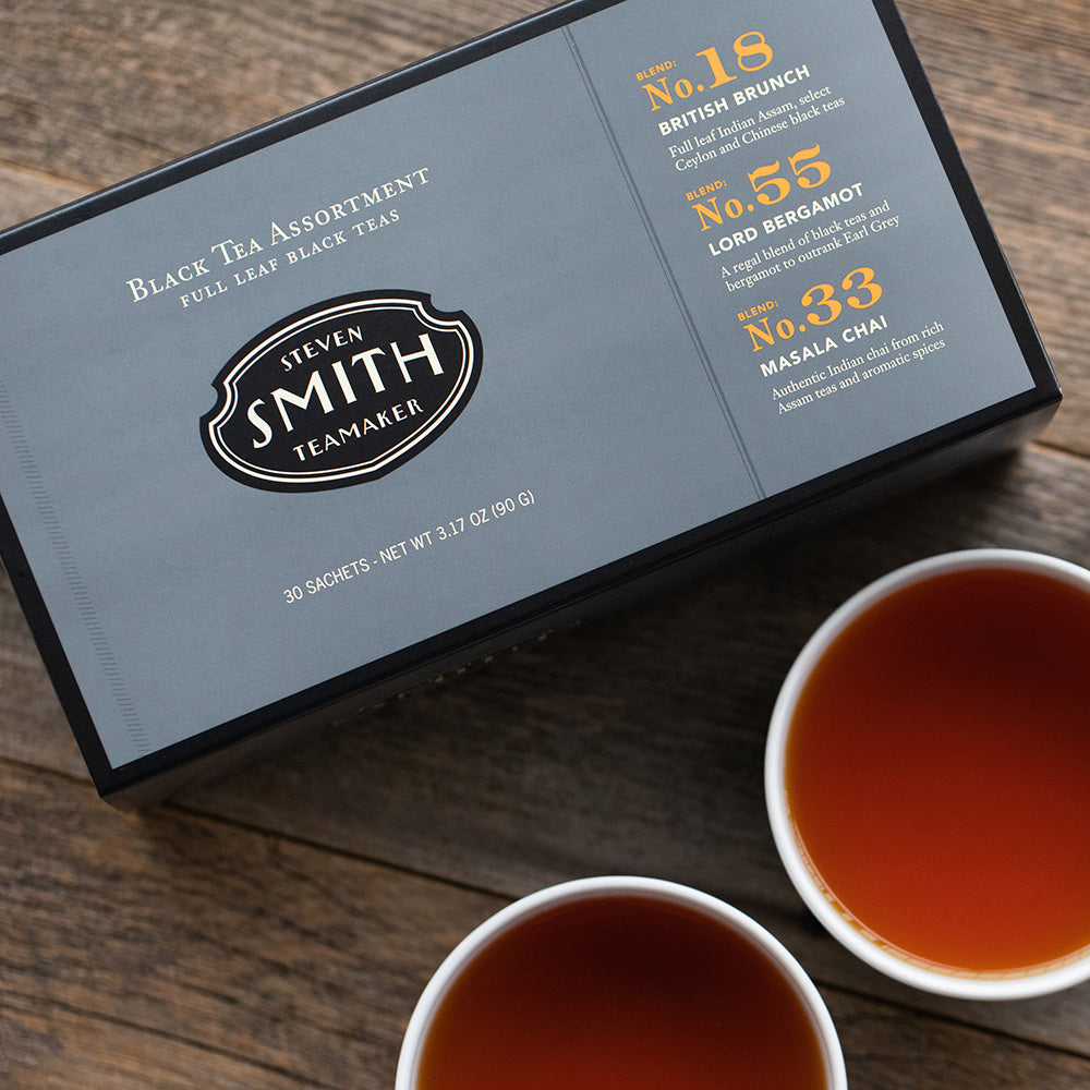 Grey box with black trim on a wooden table next two porcelain cups filled with black tea.