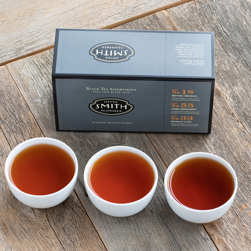 Grey box with black trim on a wooden table next three porcelain cups filled with black tea.