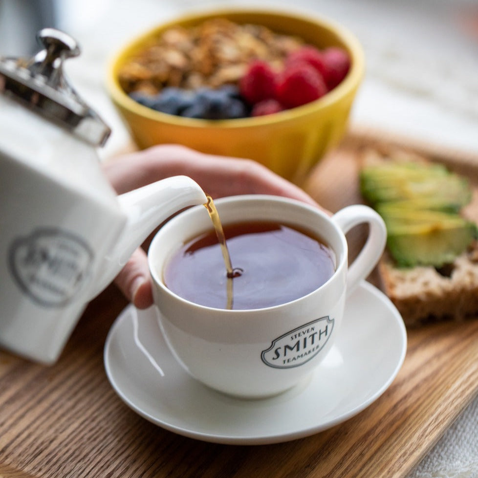 Teacup filled with  black tea next toast with avocdo and granola.