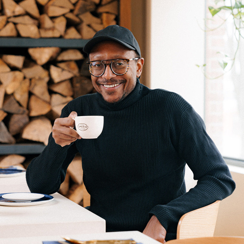 Chef Gregory Gourdet sitting at a white table smiling with a cup of tea.