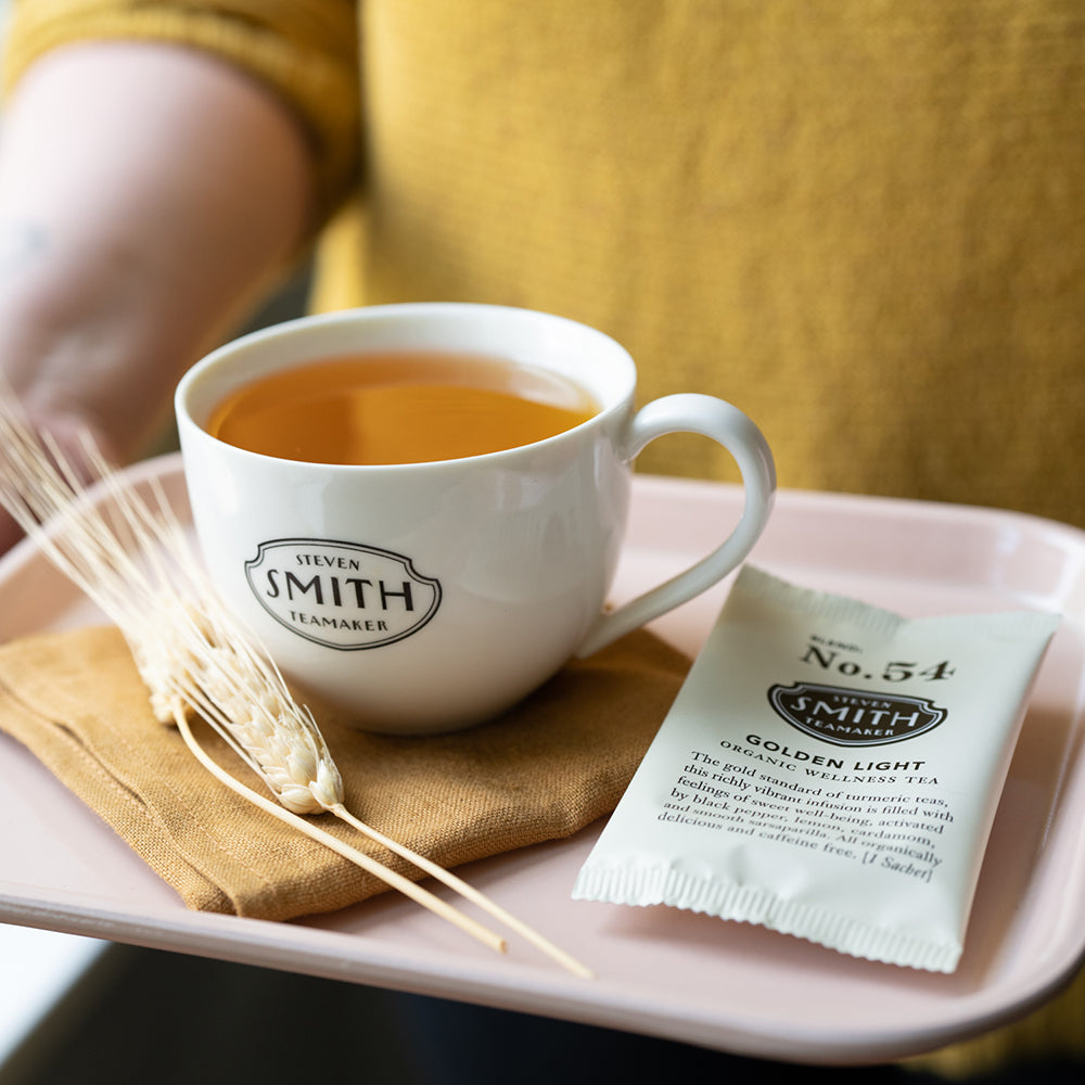 Person holding tray with white porcelain cup filled with orange golden light tea.