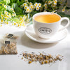 Porcelain cup filled with Lullaby organic wellness tea next to fresh chamomile flowers.