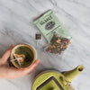 Table with sachet of Rose City Genmaicha, green teapot and ceramic brown cup filled with tea.