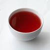 White porcelain cup on white background filled with red hibiscus tea.