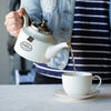 Person pouring tea into white porcelain cup from a white porcelain teapot.