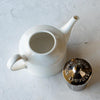 White porcelain teapot with stainless steel lid sitting next to it.