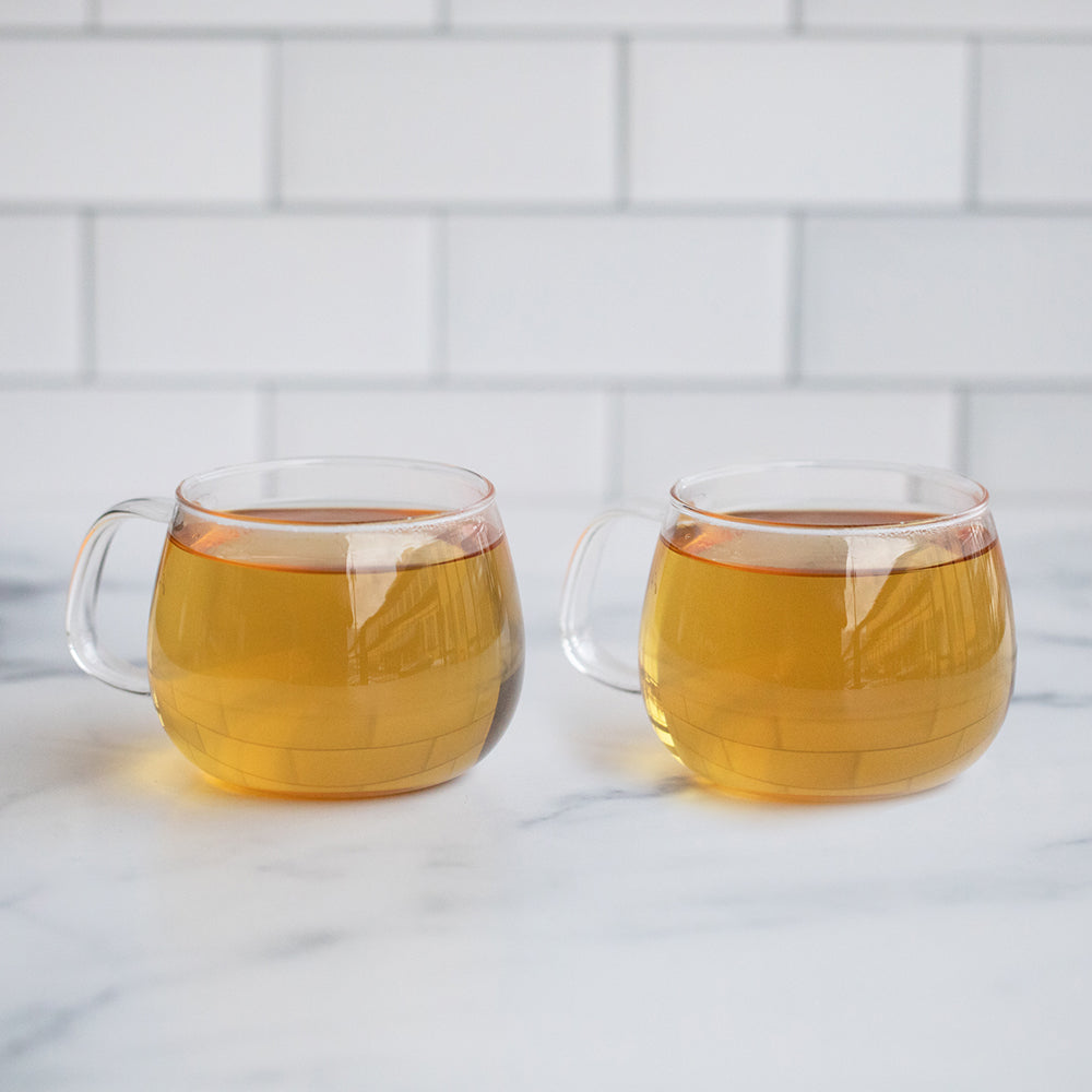 Two glass cups filled with light brown liquid on a marble background.
