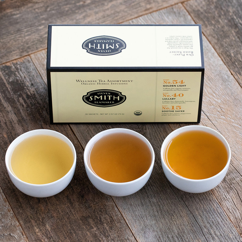 Cream box with black trim on marble background with three porcelain cups filled with tea.